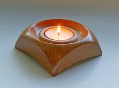 a small wooden candle holder with a lit candle in the center on a white surface