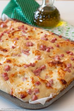 a pizza sitting on top of a pan covered in cheese and ham next to a bottle of olive oil