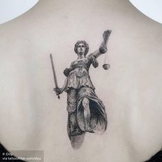 a lady justice tattoo on the back of a woman's upper back, holding two scales