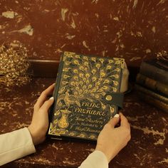 a person is holding a book on a table next to some books and other items