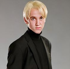 a man with blonde hair wearing a black suit and turtle neck sweater posing for a photo