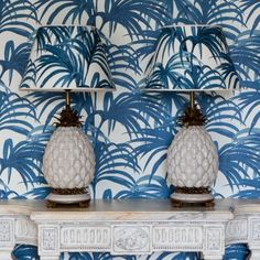 two white pineapple lamps sitting on top of a table next to a blue and white wallpaper