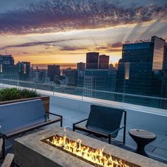 a fire pit sitting on top of a roof next to two chairs and a table