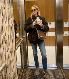 a woman standing in an elevator taking a selfie with her cell phone and purse