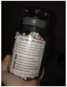 a person holding a jar filled with lots of colorful beads and writing on the label