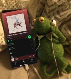 a green stuffed animal sitting on top of a bed next to an mp3 player