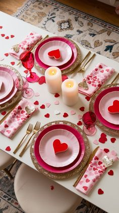 the table is set for valentine's day with pink and gold plates, silverware, and candles