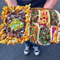 a person holding two trays of food with different types of foods on them and fries