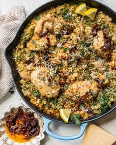 a pan filled with chicken and rice next to a bowl of lemon wedged parmesan cheese