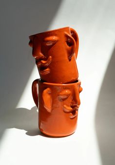 two orange mugs sitting side by side on a white surface, one with faces painted on it