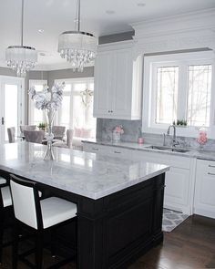 a large kitchen with white cabinets and marble counter tops, chandelier above the island