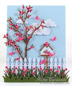 a card with pink flowers and a bird house in the grass next to a white picket fence