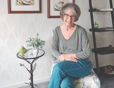 an older woman sitting on top of a chair in front of a wall with pictures