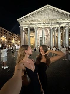 two beautiful women standing in front of an old building with columns and pillars at night