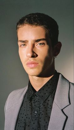 a man in a gray suit and black polka dot shirt looking at the camera with an intense look on his face