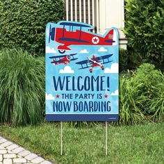 a welcome sign is in front of some bushes and grass, with an airplane painted on it