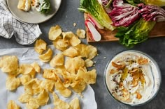 chips, salad and dip are on the table next to plates with different types of food