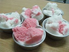 four small tins filled with pink and white dessert items on a wooden table top