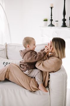 a woman sitting on top of a white couch holding a small child in her lap