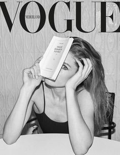 a woman sitting at a table with a book on her head while reading the magazine