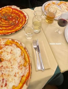 two pizzas sitting on top of a table next to silverware and wine glasses