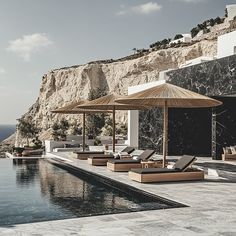 an outdoor swimming pool with lounge chairs and umbrellas next to it, overlooking the ocean