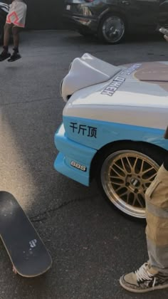 a person standing next to a skateboard in front of a blue and white car