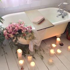 there is a bathtub with candles and flowers on the floor in front of it