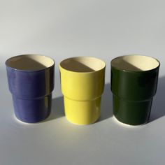 three different colored cups sitting next to each other on a white surface with one empty cup in the middle