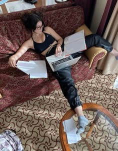 a woman sitting on top of a couch with papers in her lap and holding a laptop