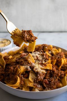 a fork full of pasta with meat and sauce on the side in a white bowl