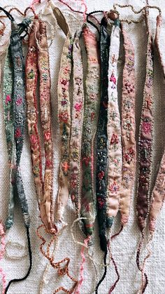 many different colored ribbons are hanging on a white cloth tablecloth with beads attached to them