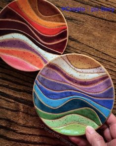 a hand holding two colorful plates on top of a wooden table