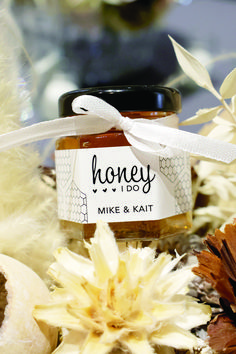 a jar of honey sitting on top of some flowers and feathers with a ribbon around it