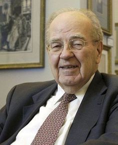 an older man in a suit and tie is sitting down with his arms folded out