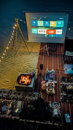 an outdoor bbq with food and drinks on the ground next to it, in front of a large screen