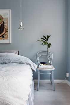 a bedroom with blue walls and white bedding has a plant on the nightstand next to it