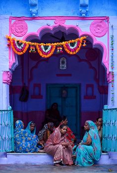 three women sitting on a bench in front of a blue and pink building with decorations