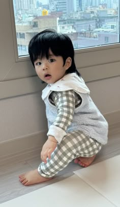 a small child sitting on the floor in front of a window with cityscape