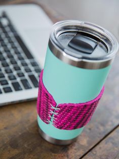 a laptop computer sitting on top of a wooden table next to a pink and blue cup