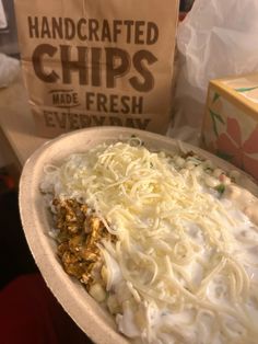 a bowl filled with noodles and cheese on top of a table next to a bag of chips