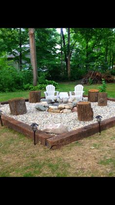 a fire pit with chairs around it in the middle of some grass and trees behind it