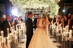 a bride and groom are standing in front of candles at their wedding ceremony as guests look on