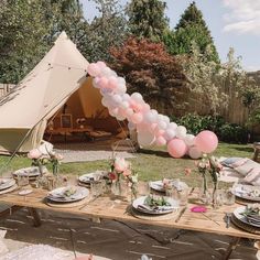 a table set up for a party with pink and white balloons, plates and utensils