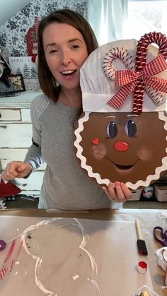 a woman is holding up a gingerbread man shaped cake with icing on it