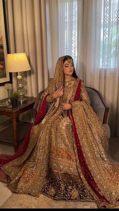 a woman sitting in a chair wearing a gold and red bridal gown