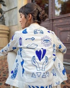 a woman walking down the street wearing a white jacket with blue drawings and symbols on it