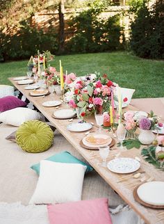 a long table with plates and candles on it in the middle of a yard area