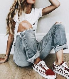 a woman sitting on the floor with her legs crossed and wearing red converse shoes,