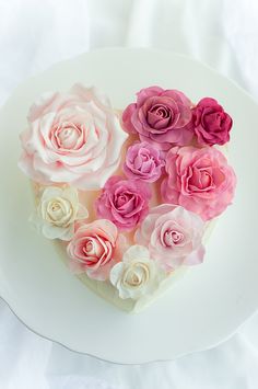 a heart shaped cake with pink and white flowers on it's top, sitting on a plate